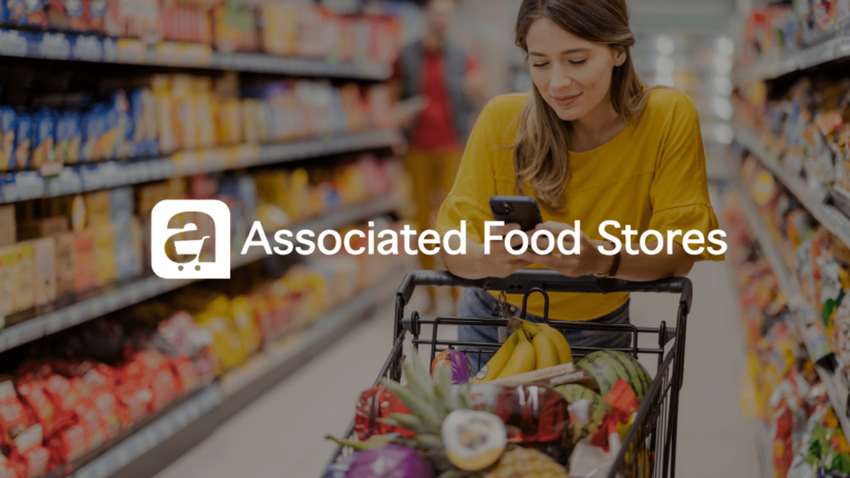 An image showing a white woman with longer light brown hair wearing jeans and a yellow short sleeve blouse browses on her smart phone while leaning on a grocery cart full of fruit in the middle of a grocery store aisle.