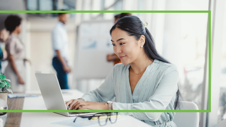 Businesswoman busy working on laptop computer at office with colleagues in the background